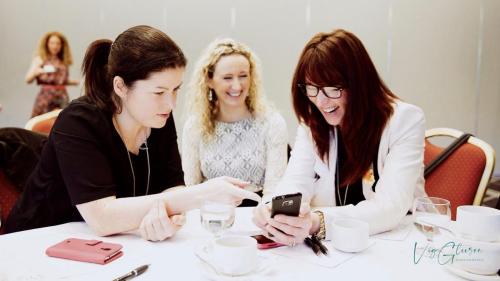 Three Irish women around a conference table, laughing, looking at a phone screen. Networking and business EVENT PHOTOGRAPHY by Vig Gleeson